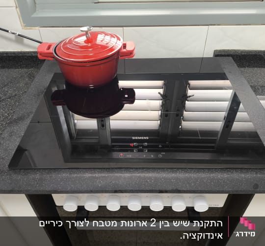 משטח שיש כהה עם סיר אדום על כיריים